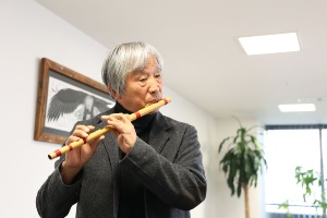中国で買った横笛を吹く辰野氏(左)、横笛セットの奥にある3本は、樹脂や竹で辰野氏が自作したもの(右)