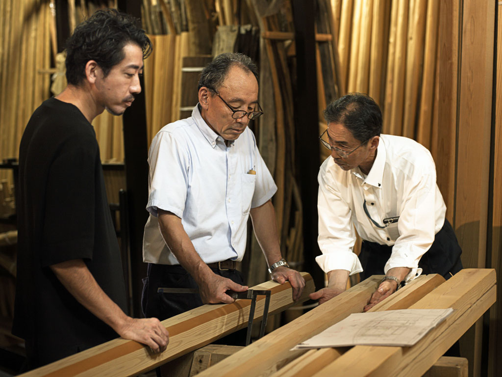 キャンパス内に建設中の茶室に使う木材（北山杉磨丸太の面皮柱）について、面（ツラ）の付け方を検討しているところ。写真左から、建築家の三井嶺氏、北山杉を育てている銘木の生産者、数寄屋大工の棟梁 　写真提供／伊藤穰一氏