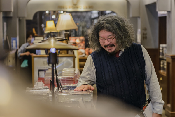 「梟書茶房」入り口にある「ふくろう文庫」に立つ柳下さん。(写真=猪俣 博史)