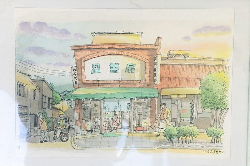 改装前の忍書房（2017年）のイラスト。赤れんがと緑の看板文字が印象的だった。よく見ると行田でロケが行われたドラマ『陸王』の文字が見える。「元編集者の村上健さんに描いていただきました。映画『騙し絵の牙』の高野書店として映った外観がしのばれます」