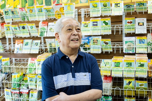 タネ袋の陳列棚を背景に語る野口さん タネ袋の陳列棚を背景に語る野口さん