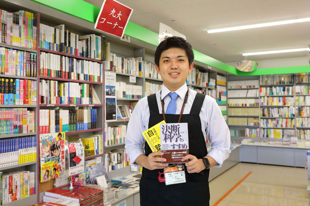 九州大学生活協同組合皎皎舎店の木原悠駿さん。手にしているのはお薦めの『18歳からの自炊塾』と『決断科学のすすめ』